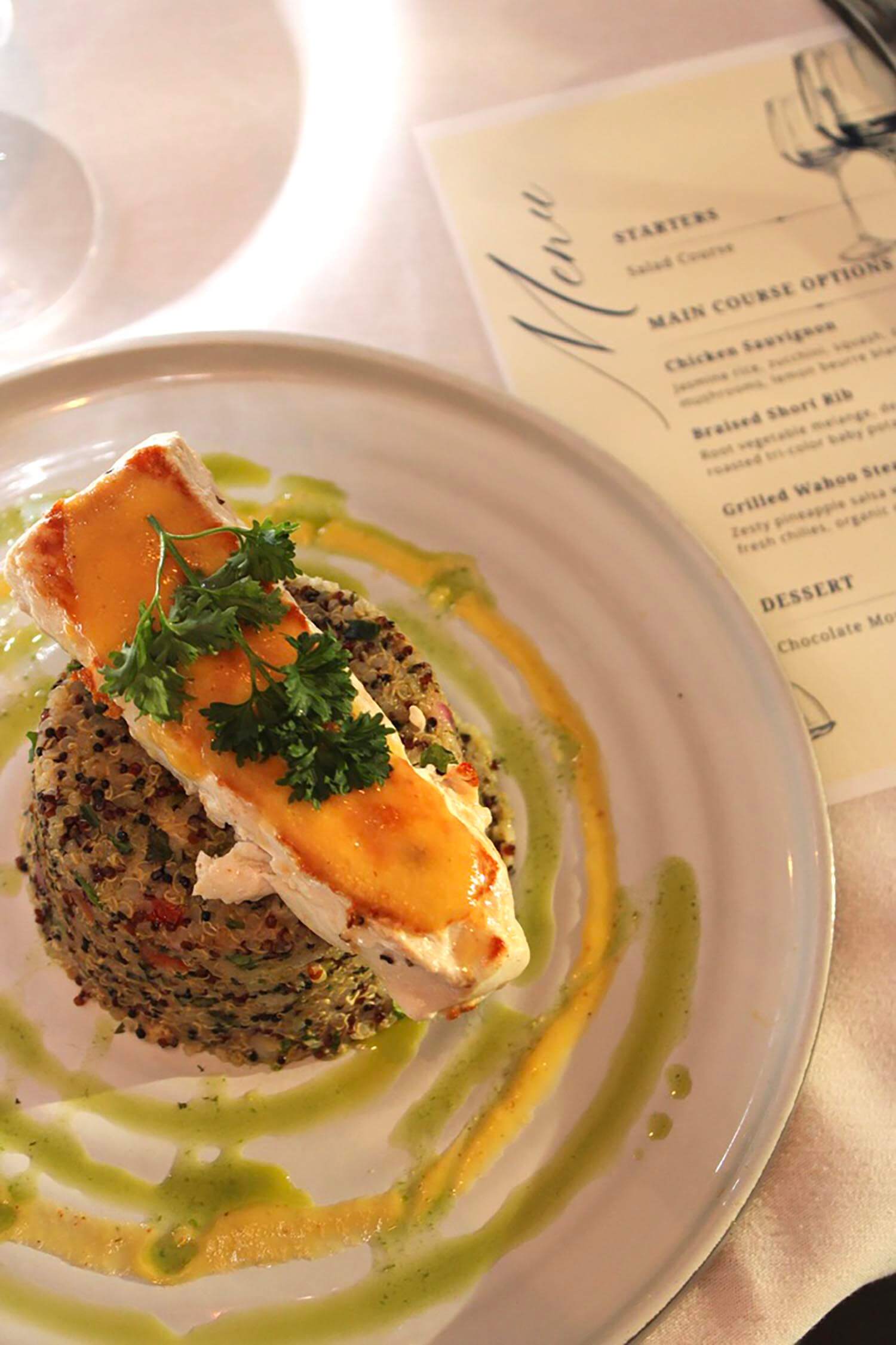 Grilled salmon fillet topped with parsley on seasoned quinoa with green and yellow sauce swirls.